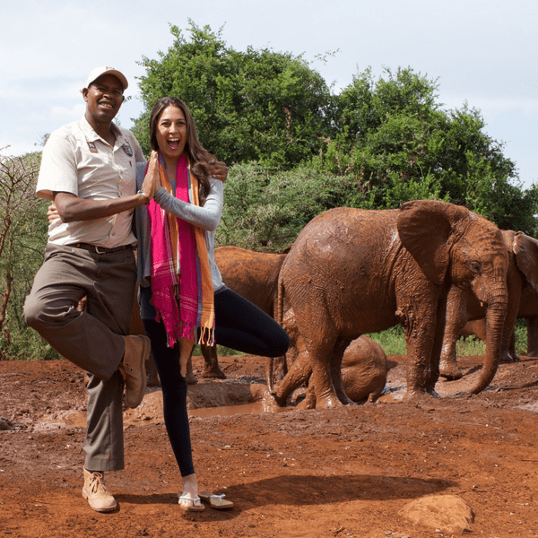 Two people connect in tree pose with elephants in the background on this Kenya yoga retreat with The Travel Yogi