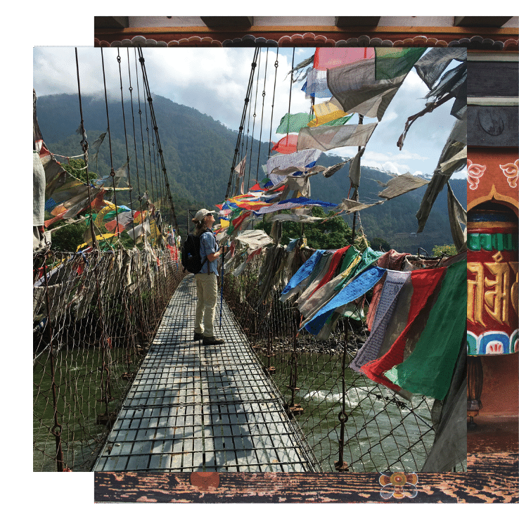 Man hikes on a bridge and admires prayer flags floating in the wind on a Bhutan yoga retreat with The Travel Yogi