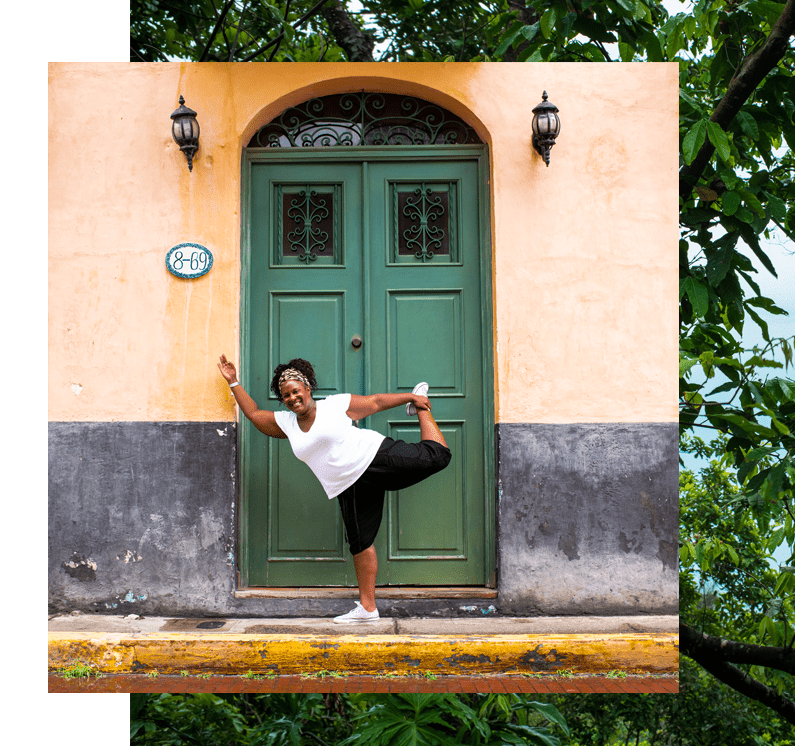 A woman does dancer pose in front of a green door. Learn about this yoga retreat in Panama with The Travel Yogi