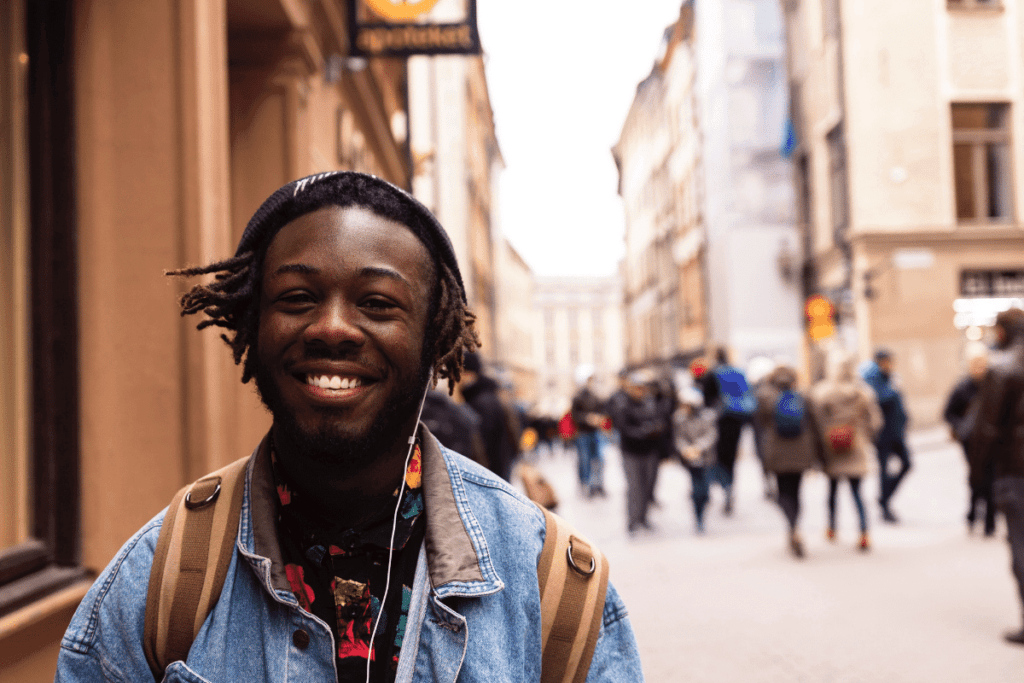 Man walks on a busy street with a backpack and a big smile. Learn why travel is good for your mental health with The Travel Yogi.