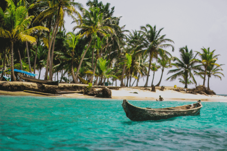 Canoe floating on green ocean waters near a sandy beach. Here are 10 bucket list travel destinations with The Travel Yogi. Photo credit: Angel Silva