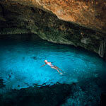 Woman swims in an azure cenote. Explore Mérida on this yoga retreat in Mexico with The Travel Yogi.