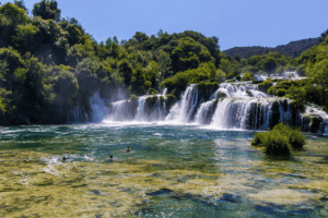 Rushing waterfalls and emerald pools with swimmers at Krka Waterfalls National Park in Croatia with The Travel Yogi.