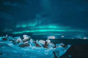 Landscape photo of rocks in the snow and Iceland northern lights. Experience with The Travel Yogi.