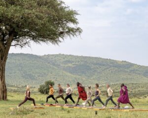 People and Maasai warriors doing yoga on wooden platforms in the bush in the Masai Mara.