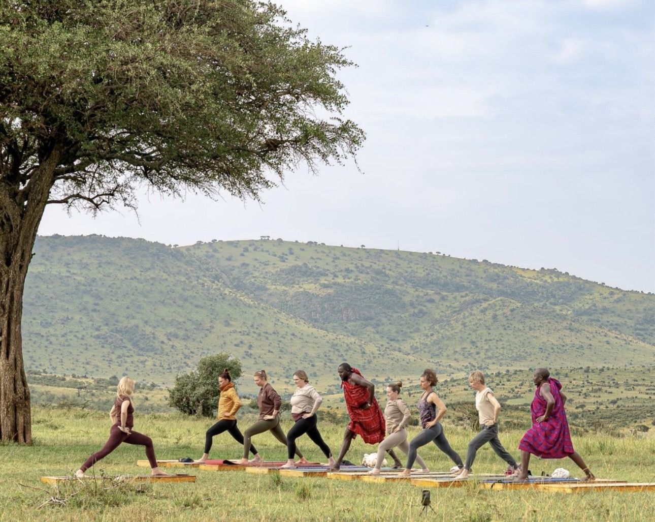 People and Maasai warriors doing yoga on wooden platforms in the bush in the Masai Mara.