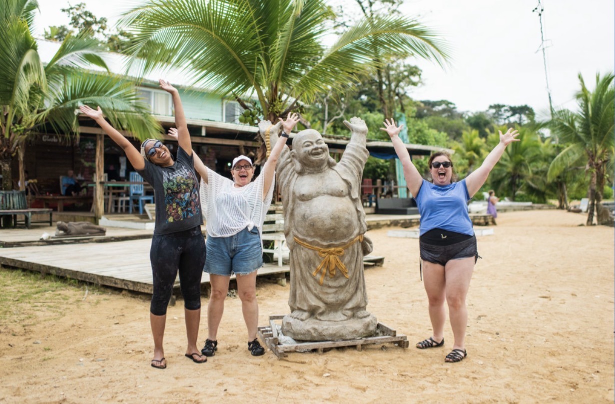 Travelers throwing their hands up in Panama next to a statue